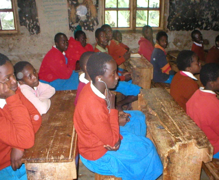 Students in red sweaters and blue skirts or pants sitting at desks in their classroom